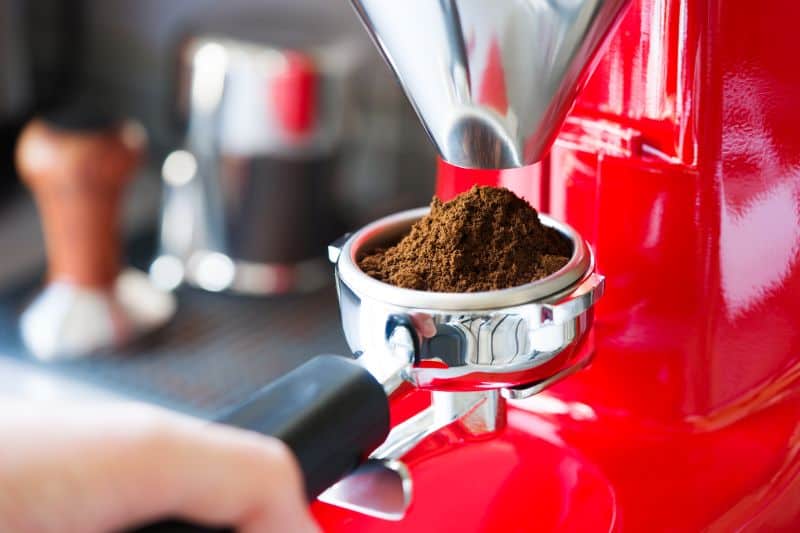 Red coffee grinder with portafilter filled with fresh coffee grounds.