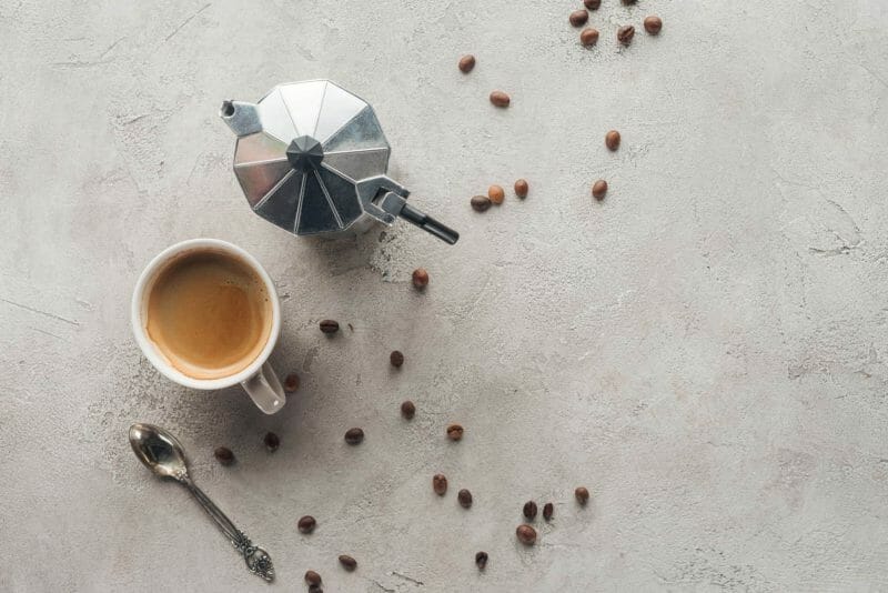 Flat lay of moka pot and coffee cup with coffee beans and spoon.