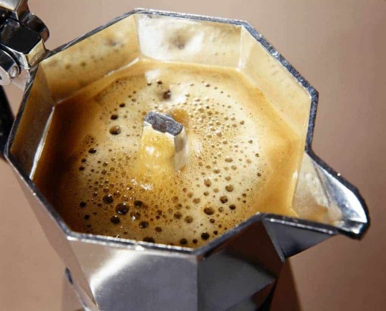Close up of top compartment of moka pot brewing coffee.