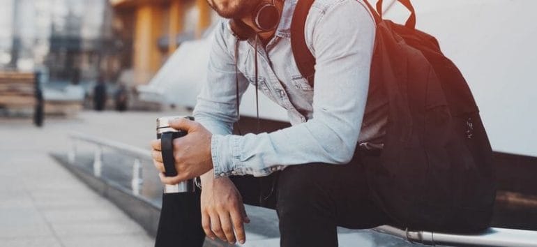 Guy with backpack holding coffee thermo mug in hands