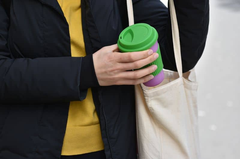 Woman holding reusable coffee cup putting into a bag outdoors. Zero waste. Sustainable lifestyle