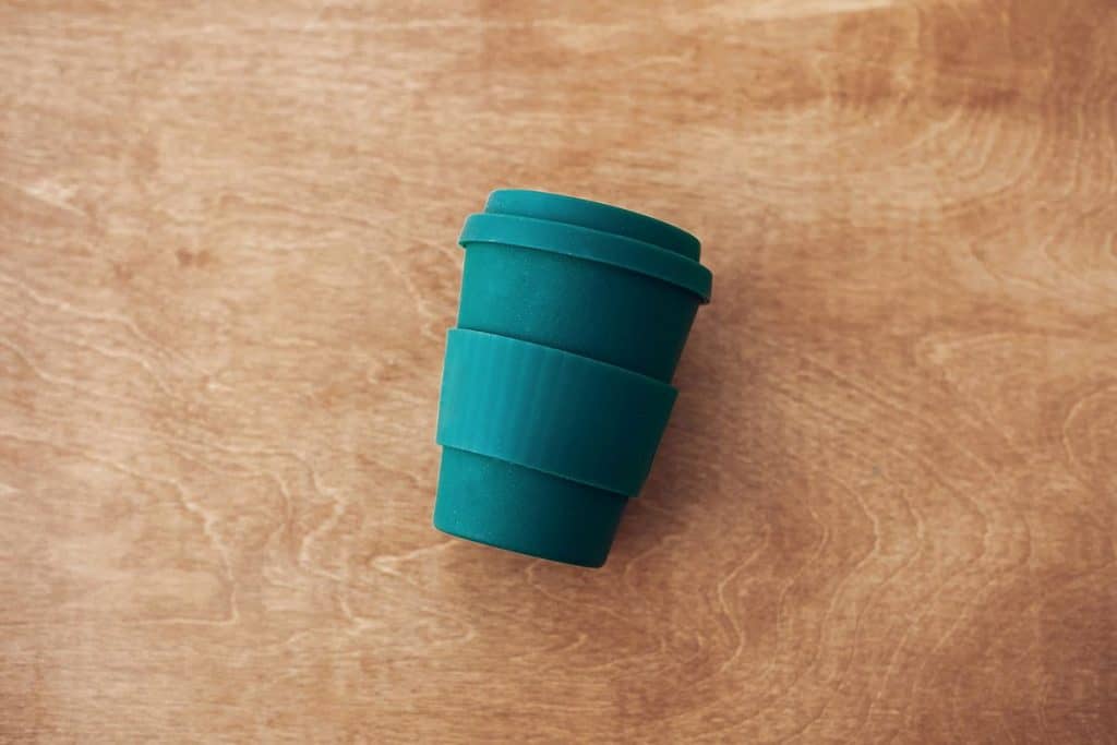 Stylish reusable eco coffee cup on wooden background, flat lay
