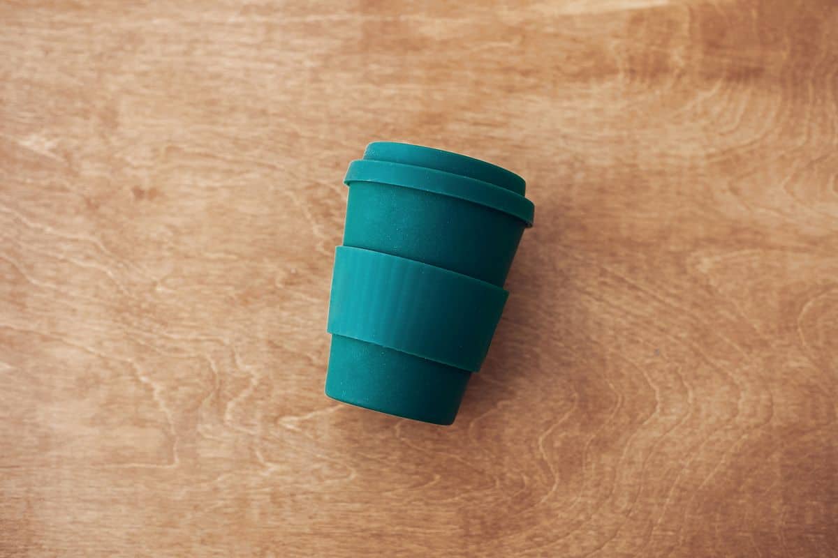 Stylish reusable eco coffee cup on wooden background, flat lay