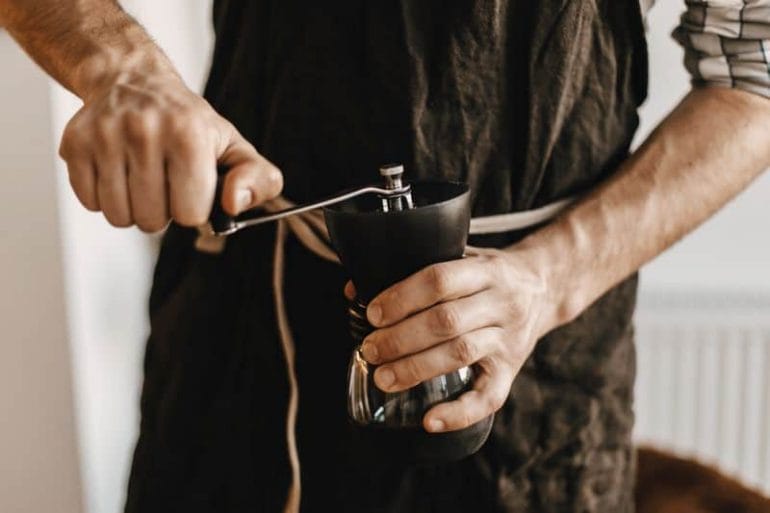Hands holding coffee grinder hand crank.