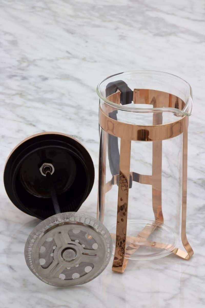Empty glass french press coffee maker with stainless steel filter and plunger.