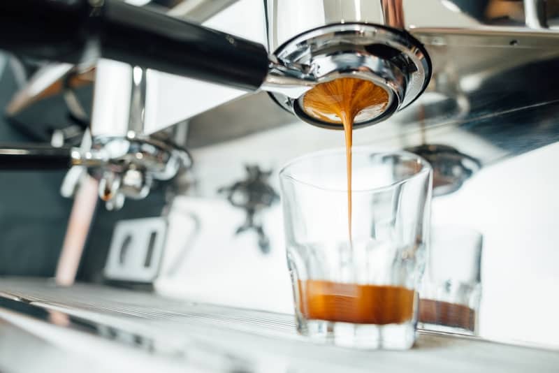 finish of the espresso extraction process from bottomless portafilter in a glass cup, side view