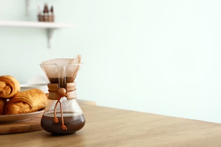 Chemex pour over coffee maker with hot coffee on wooden table.