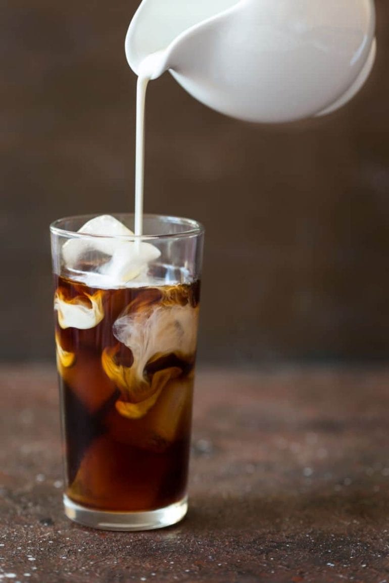 Iced cold brew coffee in a tall glass with cream poured over.