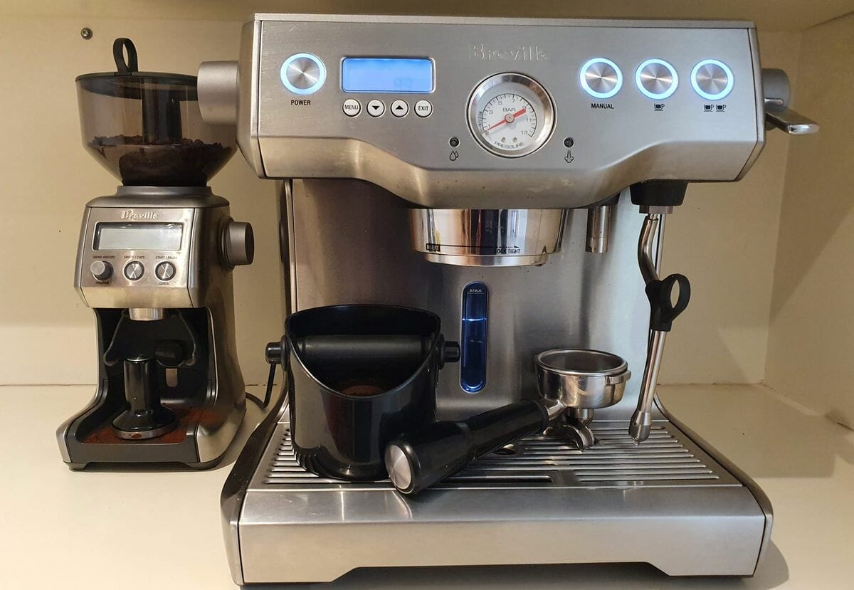 Grindenstein knock box black sitting on espresso machine drip tray.