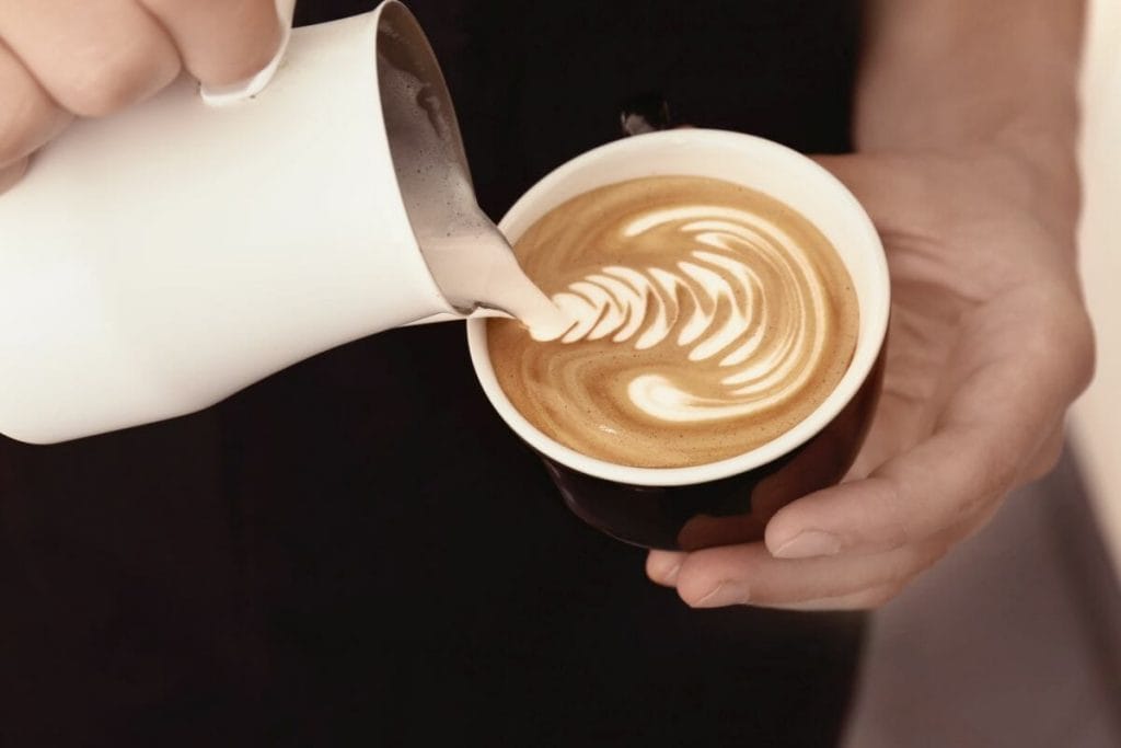 pouring frothed milk into coffee cup with milk pitcher.