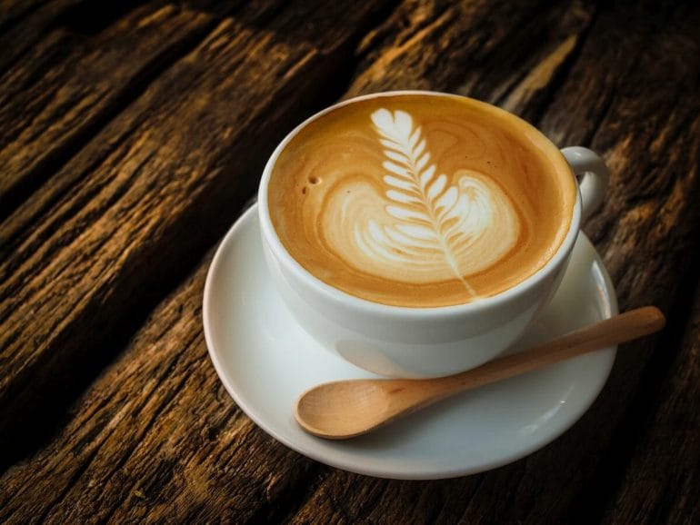 white coffee cup with latte art on wooden bench top.