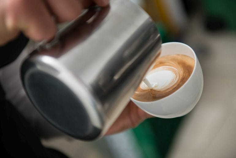Barista pouring milk into the cup of coffee making latte art.
