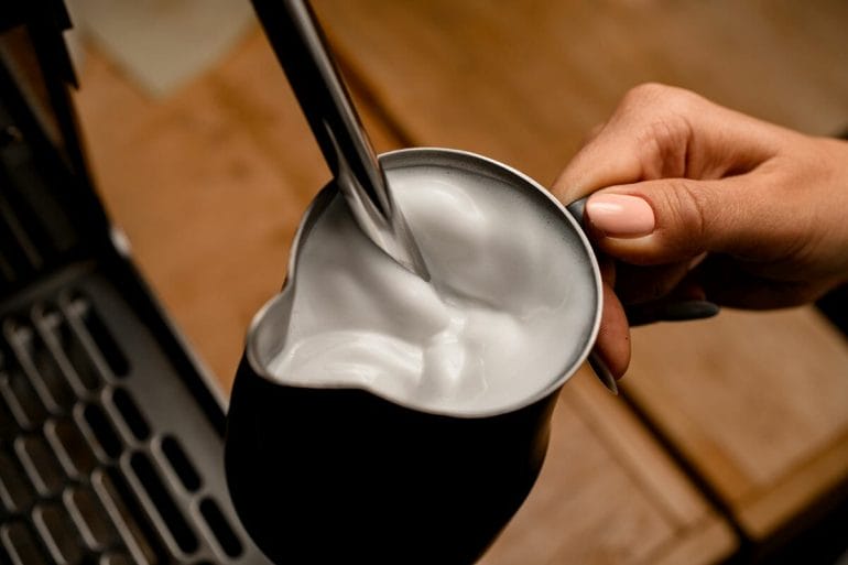 high angle view of fresh steamed milk foam in jug in woman's hand.