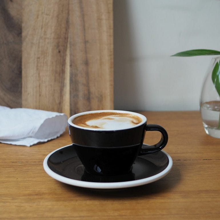 magic coffee in black cup and saucer on wooden bench top.