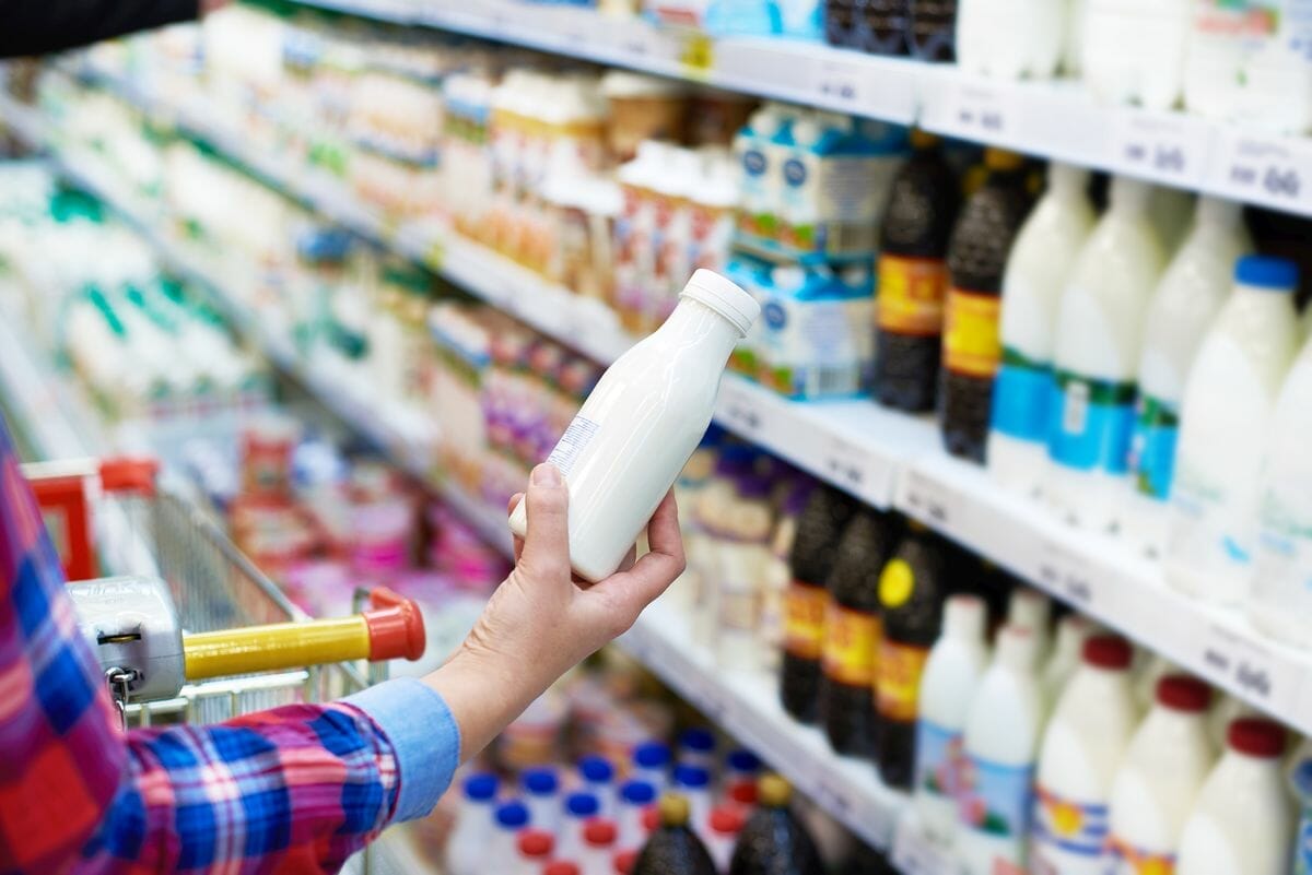 Woman holding milk container in supermarket with other types of milk.