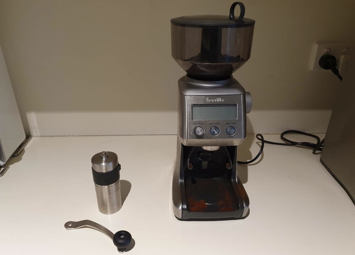 small hand coffee grinder next to automatic coffee grinder on bench top.