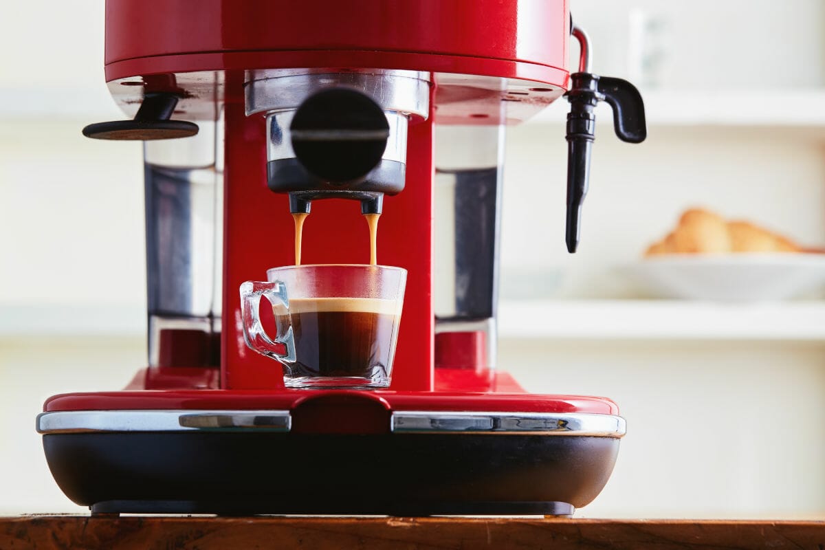 Closeup of red espresso coffee machine extracting espresso into a glass cup.