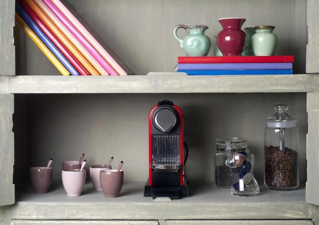 Coffee capsule machine on shelf with cups and coffee beans and pods.