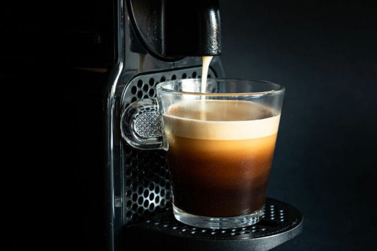 Black nespresso coffee pod machine extracting espresso into glass coffee cup.