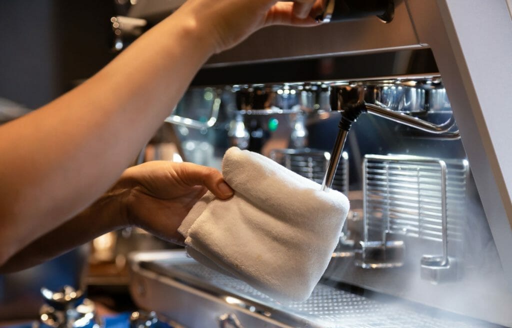 hand of barista cleaning milk frother on espresso machine.