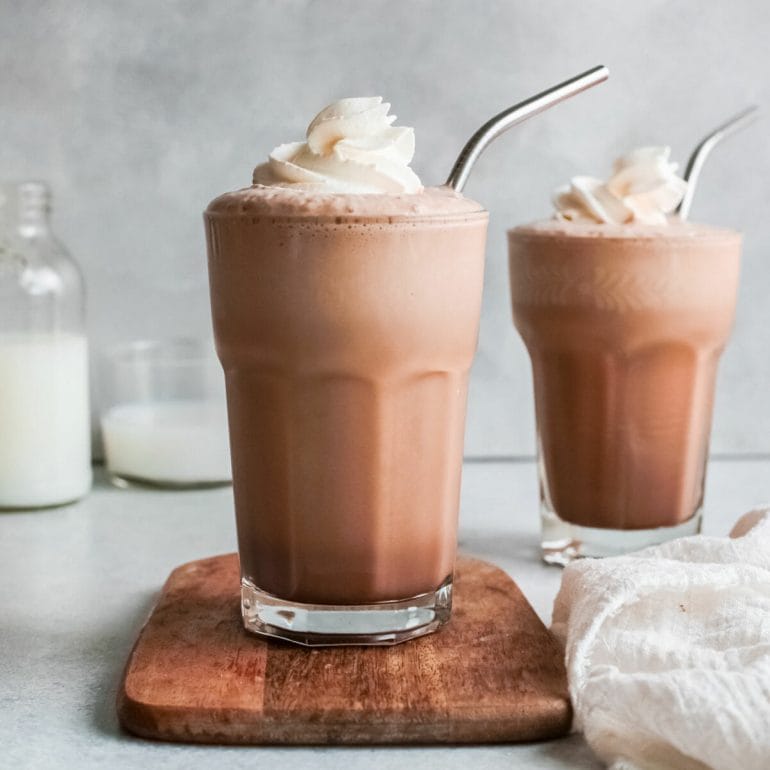 Closeup of iced coffee nutella frappe in glass with straw on table.