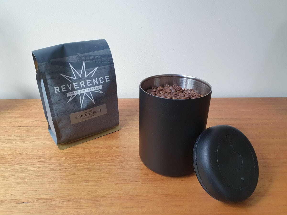 Airscape coffee storage container filled with coffee beans with bag of coffee beans alongside.